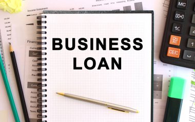 Hesap makinesi ve ofis malzemelerinin yanında beyaz bir arkaplanda BUSINESS kredisi yazılı not. İş konsepti.