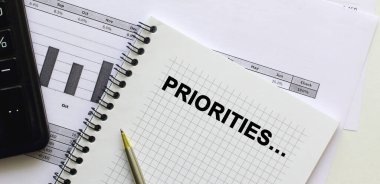 Ofis masasındaki mali tabloların üzerinde duran bir not defterinin sayfasına özel metinler yaz. Hesap makinesinin yanında. İş konsepti.