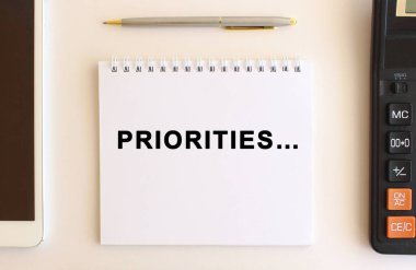 Hesap makinesi, tablet ve kalemin yanında beyaz bir arkaplan üzerinde PRIORITIES metin notları. İş konsepti.