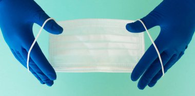 Bir çift ince mavi lateks eldiven ve beyaz arka planda yüz kalkanı. Tek kullanımlık lastik eldiven ve maske. Koruyucu denekler. İlaçlar..