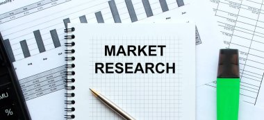 Ofis masasındaki mali tabloların üzerinde duran not defterinin sayfasına MARKET REARCH 'ı yaz. Hesap makinesinin ve işaretleyicinin yanında. İş konsepti.