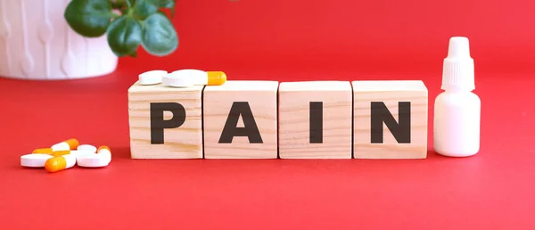 Pain 这个词是用红色背景的木制立方体和药物制成的 医疗概念 — 图库照片