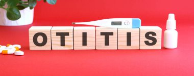 OTITIS kelimesi kırmızı arka planda tıbbi ilaçlarla birlikte tahta küplerden yapılmıştır. Tıbbi konsept.