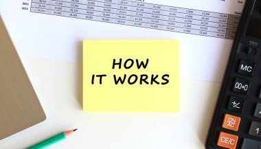 Laptopun yanındaki sarı yapışkan notlardaki yazı ve beyaz ofis masasındaki hesap makinesi. İş konsepti.