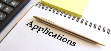 Hesap makinesi ve sarı not kağıtlarının yanında beyaz bir arkaplan üzerinde APPLICATIONS metin notları. İş konsepti.