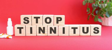 STOP TINNITUS kelimesi tıbbi ilaçlı kırmızı arka planda bulunan tahta küplerden yapılmıştır. Tıbbi konsept.