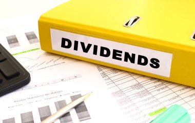 Sarı belge klasörü ofis masasının üzerinde. Bir hesap makinesine ve finans grafiklerine yakın.