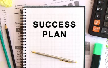 Hesap makinesi ve ofis malzemelerinin yanında beyaz bir arkaplan üzerinde SUCCESS PLAN yazılı not defteri. İş konsepti.