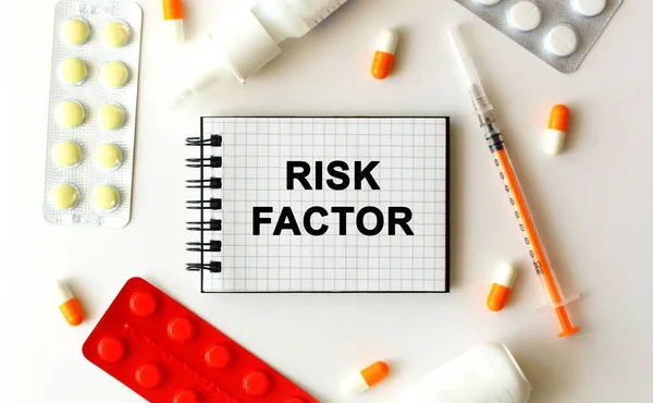 Notepad with text RISK FACTOR on a white background. Nearby are various medicines. Medical concept.