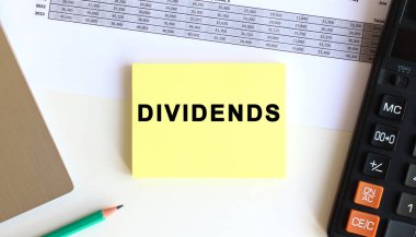 Laptopun yanındaki sarı yapışkan notlardaki yazı ve beyaz ofis masasındaki hesap makinesi..