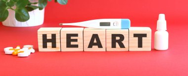 HEART kelimesi kırmızı arka planda tıbbi ilaçlarla birlikte tahta küplerden yapılmıştır..