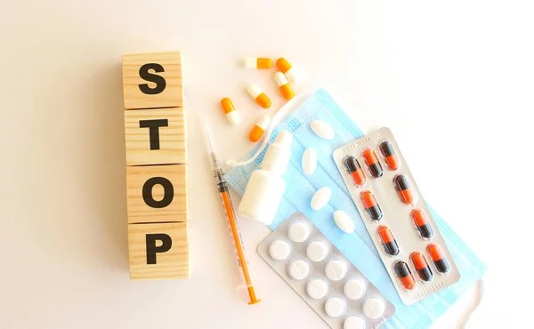 Stop一词是由白色背景的木制立方体制成的 带有医疗药物和医疗面具 — 图库照片