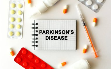 Beyaz arkaplanda PARKINSONS DISEAS mesajı olan bir not. Yakınlarda çeşitli ilaçlar var. Tıbbi konsept.