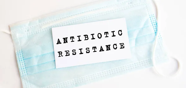 White card with the inscription Antibiotic resistanceon on a medical protective mask.