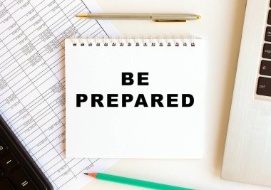 Diz üstü bilgisayar, hesap makinesi ve ofis malzemelerinin yanında beyaz bir arkaplan üzerinde hazır olun metni olan not defteri.