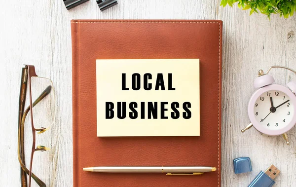 Brown notebook, sticker with the inscription LOCAL BUSINESS, pen, watch and glasses on a wooden background. Business concept.