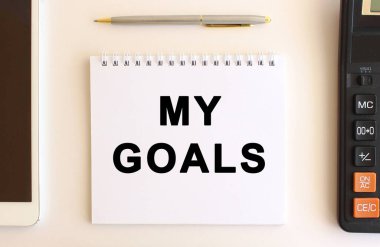 Hesap makinesi, tablet ve kalemin yanında beyaz bir arkaplan üzerinde benim hedeflerim metni ile not.