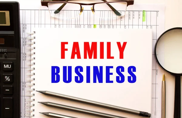 写字台上有财务文件放大镜计算器眼镜带有文本Family Business的记事本页 从上面看业务概念 — 图库照片