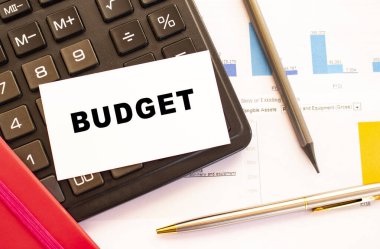 Metal kalem, hesap makinesi ve finansal tabloları olan beyaz kart üzerine metin bütçesi. İş ve mali konsept