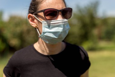 Güneşli bir günde arka bahçesinde Coronavirus salgını yüzünden maske takan güzel bir kızın portresi..