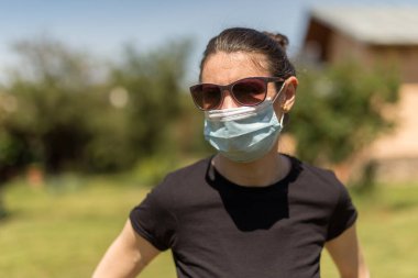 Güneşli bir günde arka bahçesinde Coronavirus salgını yüzünden maske takan güzel bir kızın portresi..