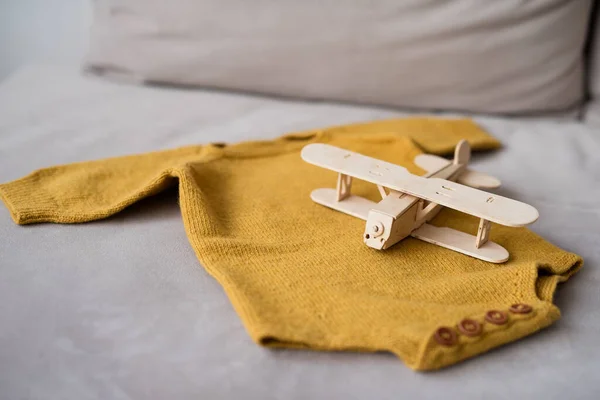 on the sofa lies a knitted bodysuit for the baby, on it lies a wooden airplane made of wood