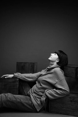 Bir kız fotoğraf stüdyosunda yerde oturuyor, dirseğini kutuların üzerine koyuyor,