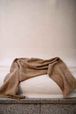 Örülmüş yün kabartmalı eşarp, elle yünden örülmüş beyaz beton bir sütunun üzerinde yatar.
