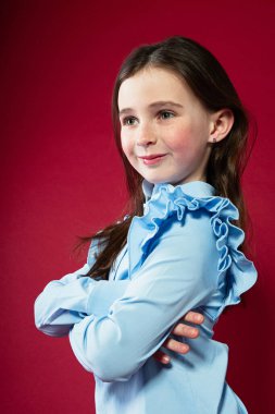 Bir kızın yakın plan portresi, ellerini katlamış ve yana bakıyor. Yüzünde bir gülümseme ve neşe var.