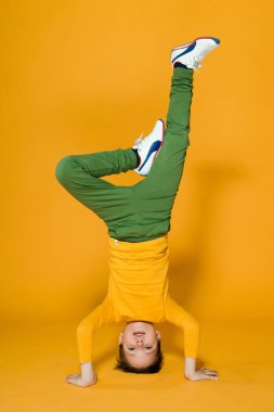  Çocuk sarı arka planda elleri üzerinde duruyor.