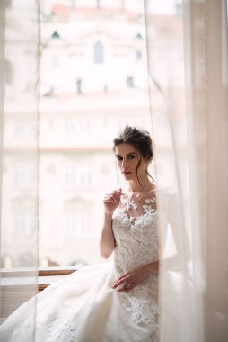 Genç gelin pencerede oturuyor, beyaz perdeler pencereyi kapatıyor, düğünden önceki kız.