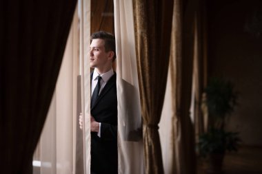 Adam pencereye yaslanmış, perdeler yüzünü kapatmış.