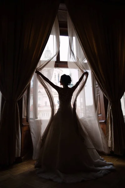 the bride in a wedding dress opens the curtains, a large window, a beautiful girl