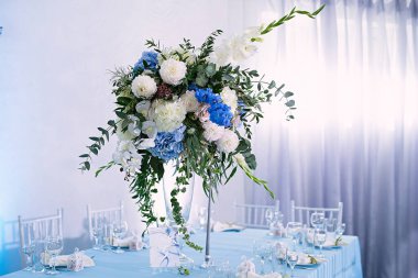 Festival masası bir vazo çiçekle süslenmiş, gardenyalı masa dekorasyonu, düğün kutlaması, mavi masa örtüsü, sandalyeler, masa düzenleme, restoranda misafirlerle akşam yemeği.