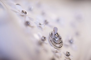 Siyah arka planda beyaz bir elbise. Elbisenin ayrıntıları yapay elmaslı kumaştan yapılmış. Çiçeklerin üzerinde yeni evliler için yüzükler var.