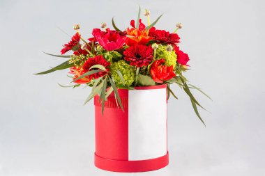 Kırmızı çiçek buketi beyaz arka plandaki bir kutuda duruyor.