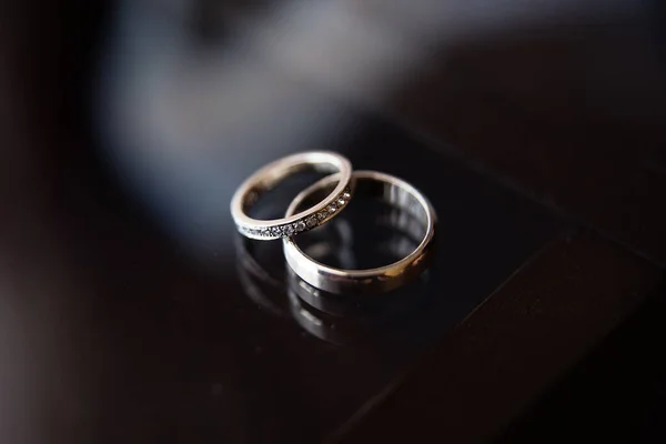 two rings for newlyweds lie on a dark background, one ring for the bride is decorated with blillants