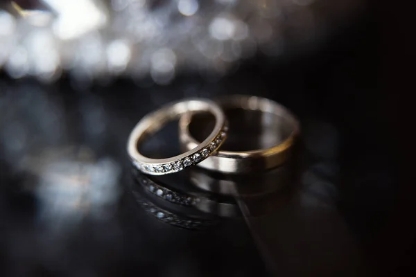 two rings for newlyweds lie on a dark background, one ring for the bride is decorated with blillants