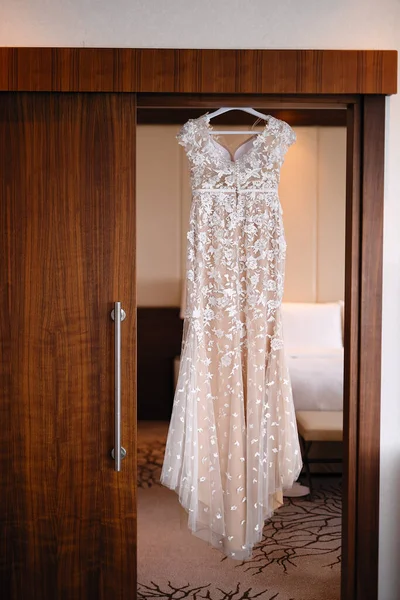 a wedding dress on a hanger hangs in the doorway, the morning of a sissy, the bride\'s outfit before the wedding, the dress is decorated with fabric flowers