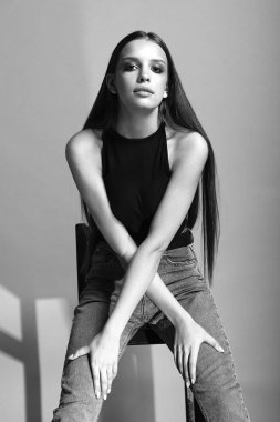 Uzun saçlı kız oturur, kollarını kavuşturur, siyah beyaz fotoğraf