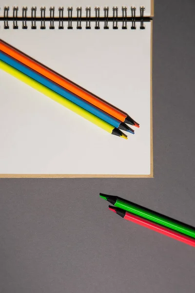 Flat notebook and bright pencils on  gray background, top view