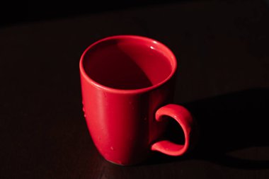 Masada kırmızı bardak, kupada şeffaf sıvı, gölgede bir nesne.