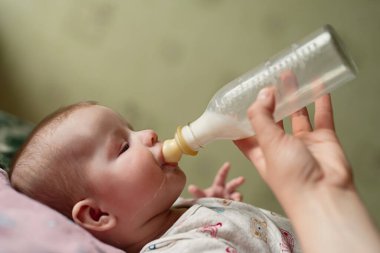 Yeni doğmuş bebek sütü şişeden yer, yemek damlaları yanaktan aşağı akar, baba bebeğe karışım verir.