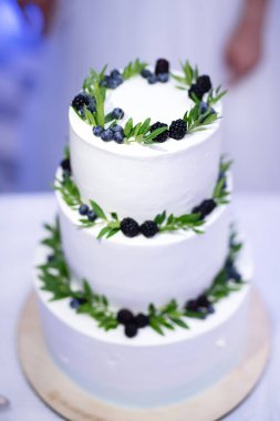Böğürtlen ve yapraklarla süslenmiş üç katlı beyaz pasta, seçici odak, düğün pastası