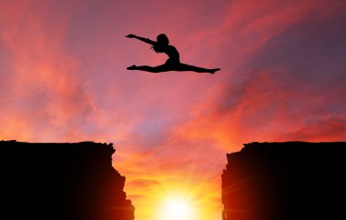 Bir split sıçrama ile dramatik gündoğumu veya günbatımı arka plan ve kopya yer tehlikeli kayalıklar üzerinde kız dansçı silüeti. İnanç, sıkıntı, risk alma fetih kavramı; meydan okuma, cesaret, azim ya da başarı.