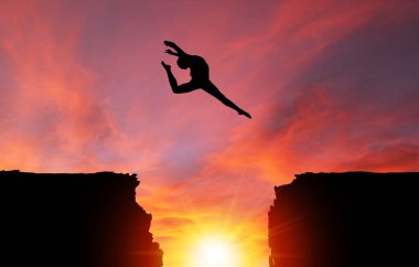 Silhouette of girl dancer in a stag split leap over dangerous cliffs with dramatic sunset or sunrise background and copy space. Concept of faith, conquering adversity, taking risk; challenge, courage, determination or achievement. clipart