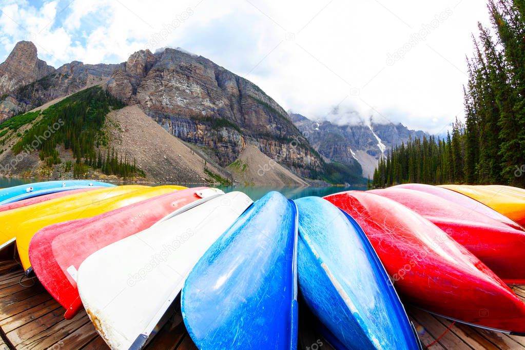 Fisheye view of a row of canoes lining the shores of Moraine Lake at Lake Louise near Banff in the Canadian Rockies, with heavy clouds descending on the Valley of Ten Peaks in the background.