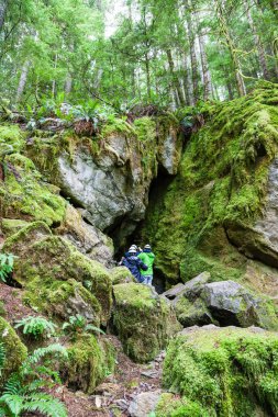 QUALICUM BEACH, CANADA - JULY 7, 2016: A group of visitors enter a cave opening at Horne Lake Caves Provincial Park on Vancouver Island's Qualicum Beach. clipart