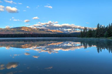 Sabah güneşi ve alçak bulutlar Rocky Dağları Annette Gölü Jasper Milli Parkı'nda Majestic Mountain ve sakin suları dağda Aquila yansımaları ile kapak.