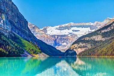 Lake Louise Banff National Park turkuaz göller buzul beslemeli ve Victoria buzul dağ içinde belgili tanımlık geçmiş. Uzaktan kırmızı Kano kürek çekmeye ziyaretçi.